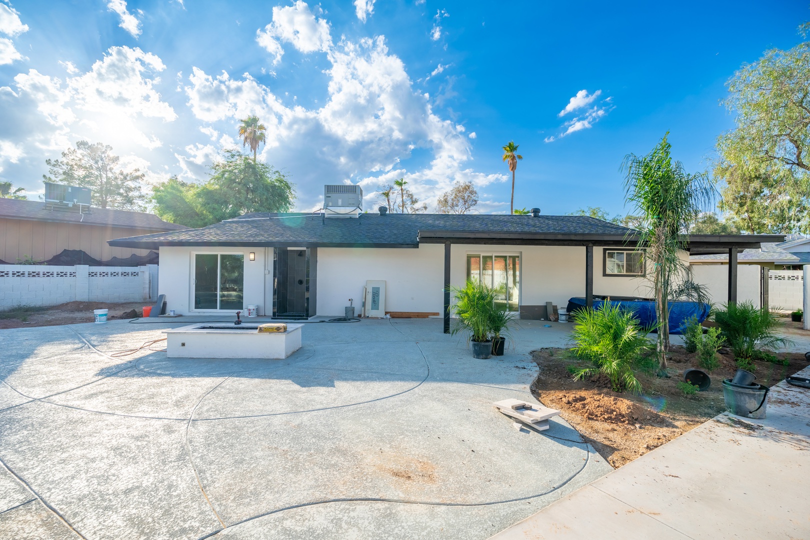 Single-story rental property with tropical landscaping and spacious outdoor areas under a bright blue sky, situated in a quiet residential neighborhood.