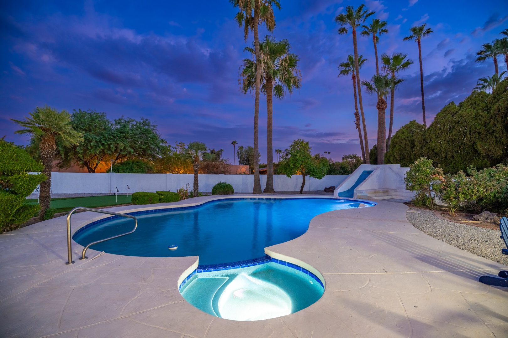 Private pool oasis with spa under swaying palms and dramatic twilight skies. The spacious deck, slide, and tropical landscaping create the perfect setting for your Palm Springs escape.