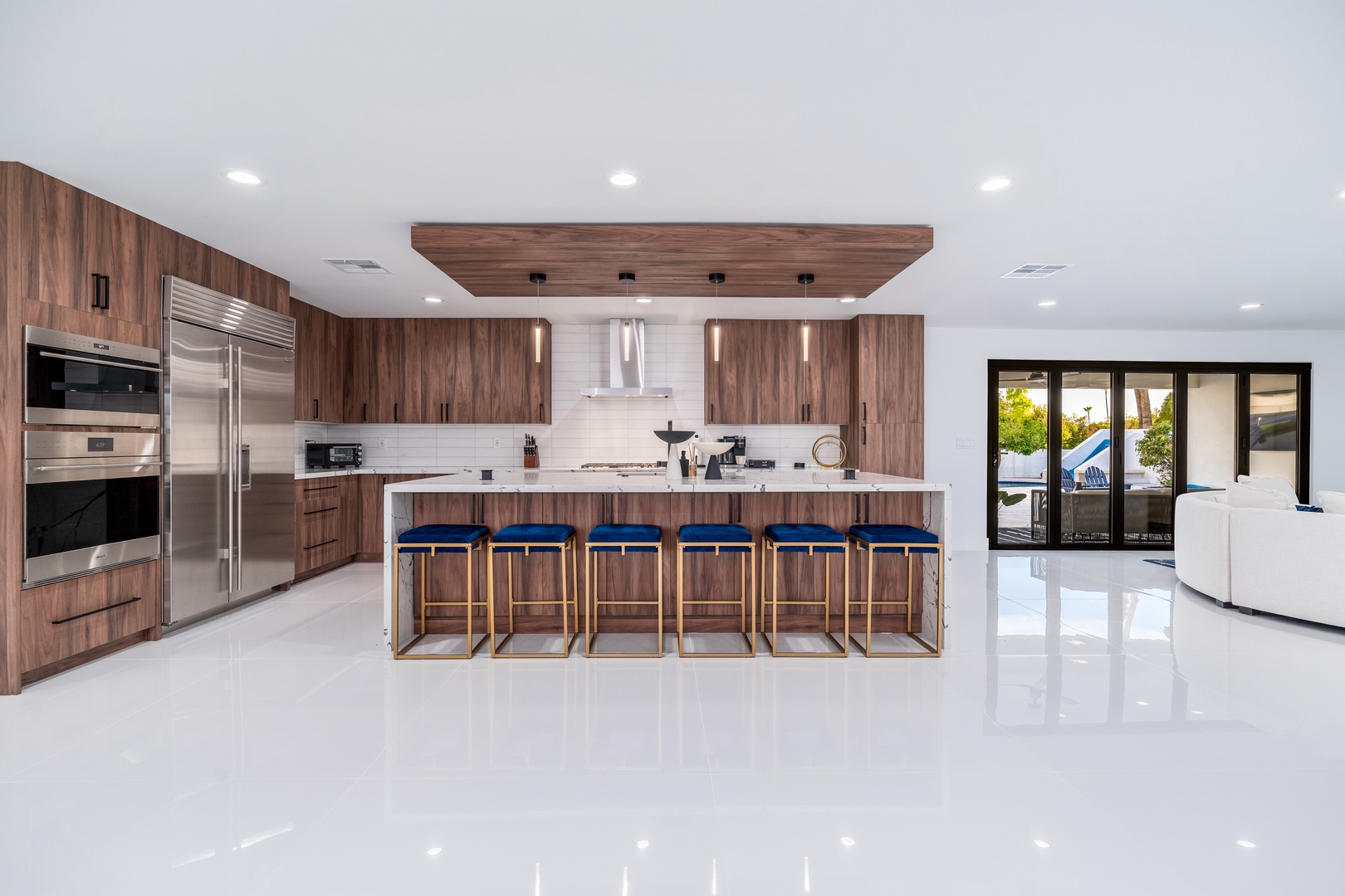 Step into your dream kitchen with rich walnut cabinetry and gleaming marble countertops, where six stylish barstools invite memorable meals and conversations by the pool.