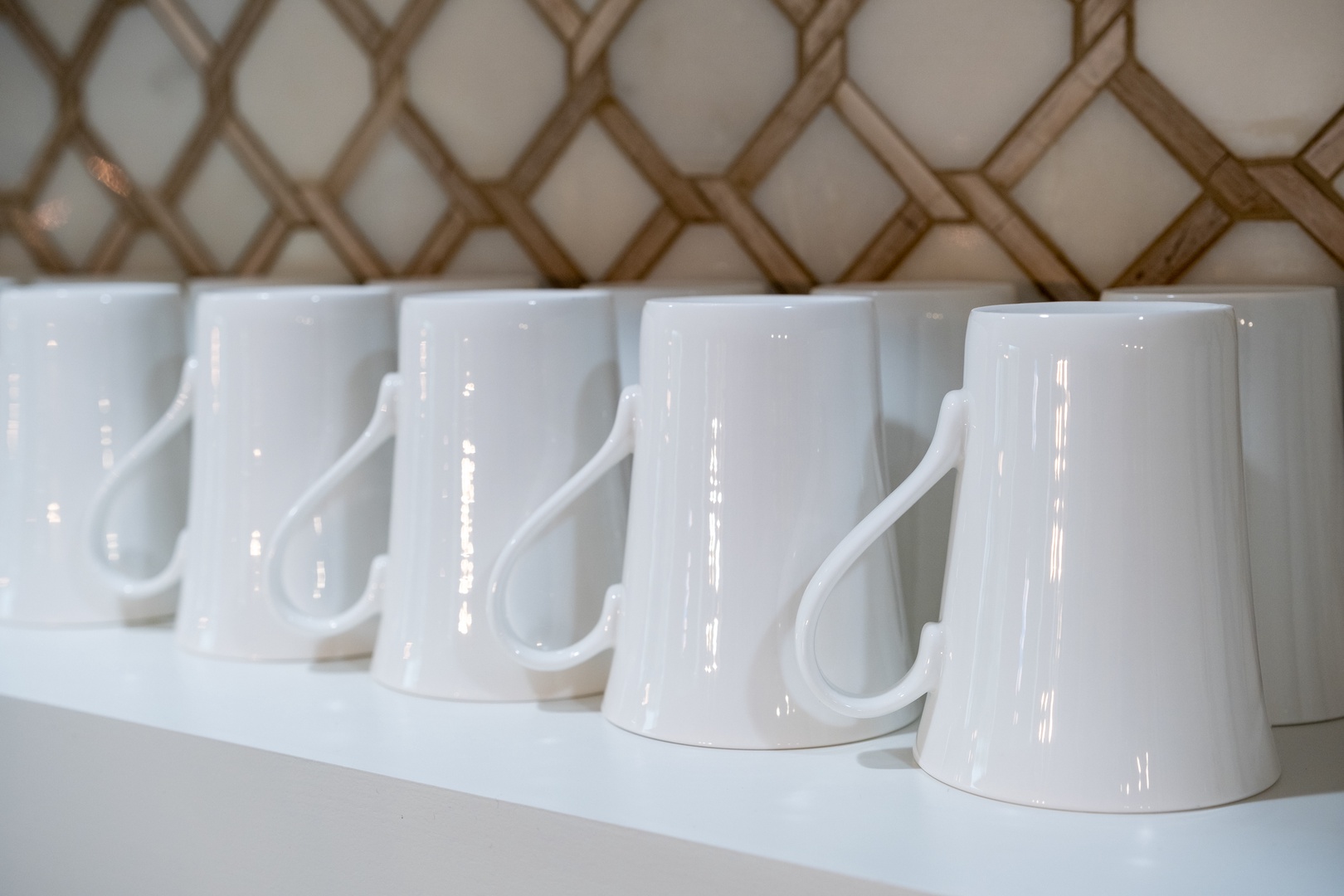 Crisp white mugs stand ready on a sleek shelf beneath elegant lattice detailing—your morning coffee or evening tea awaits in this thoughtfully designed space.