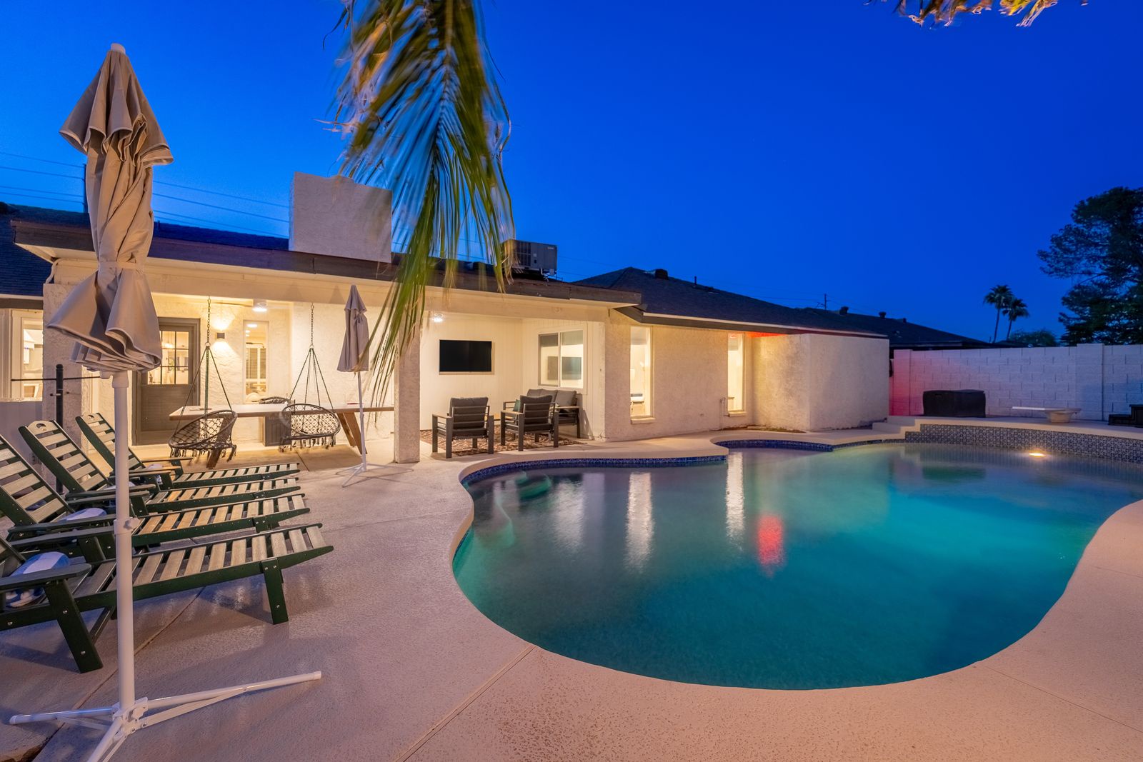 A sparkling private pool awaits in a beautifully lit outdoor space, framed by palm fronds and modern patio seating—perfect for evening relaxation under the open sky.
