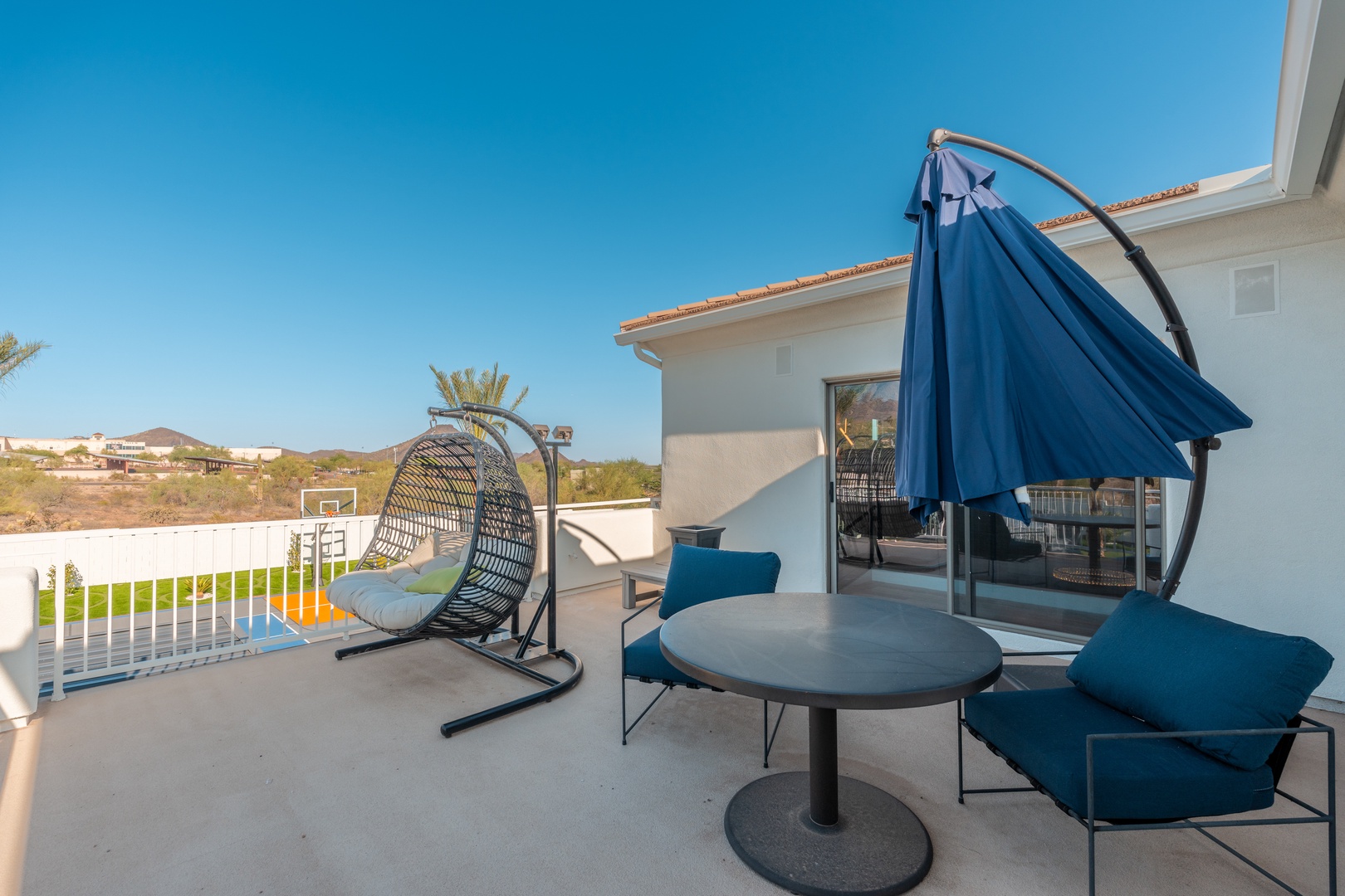 Unwind on your private balcony with modern seating and a hanging chair, overlooking scenic desert hills and clear blue skies—perfect for morning coffee or sunset relaxation.