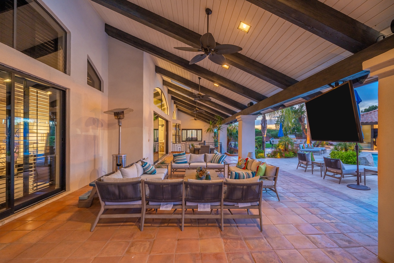 Your own private paradise awaits on this sprawling covered patio, where cozy seating invites sunset conversations under soaring wood-beam ceilings with a gentle ceiling fan overhead and poolside relaxation just steps away.