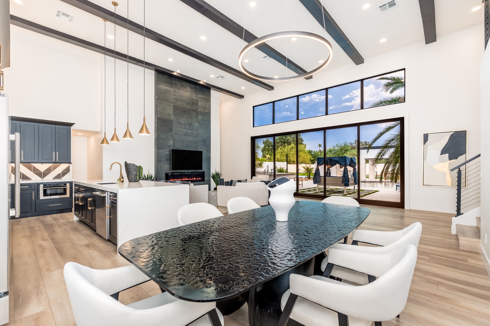 You'll love gathering around this stunning dining table beneath soaring ceilings and dramatic beams. Floor-to-ceiling glass doors frame views of the private patio, while the sleek kitchen invites easy meal prep.