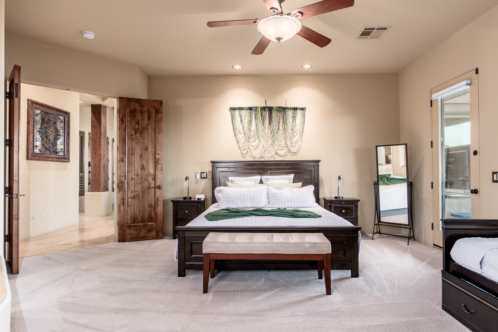 Your spacious master suite welcomes you with elegant wood furnishings, a plush king bed dressed in crisp linens, and a ceiling fan for your comfort. Natural light and stylish lighting create a serene retreat.
