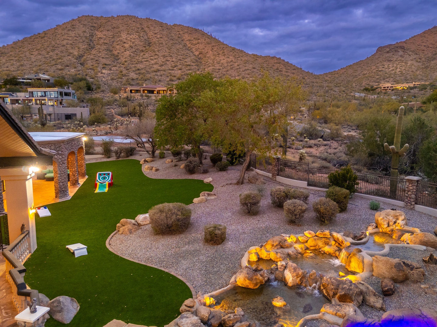 Dramatic desert landscape frames the property, with rugged mountains rising above native vegetation and neighboring homes nestled into the natural terrain.