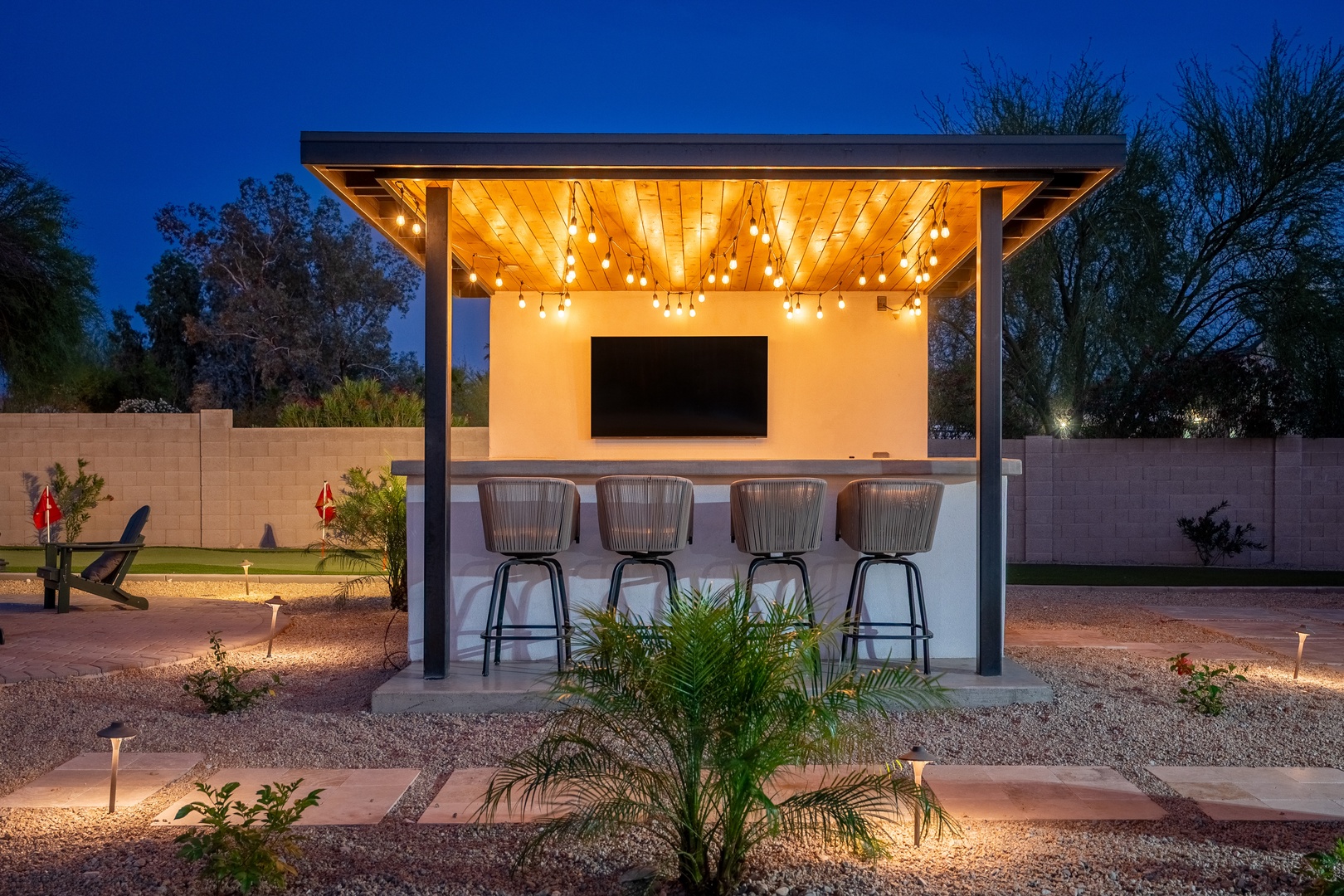 This stunning outdoor entertainment pavilion features a built-in bar with seating, ambient string lighting, and a large screen—perfect for evening gatherings under the stars.