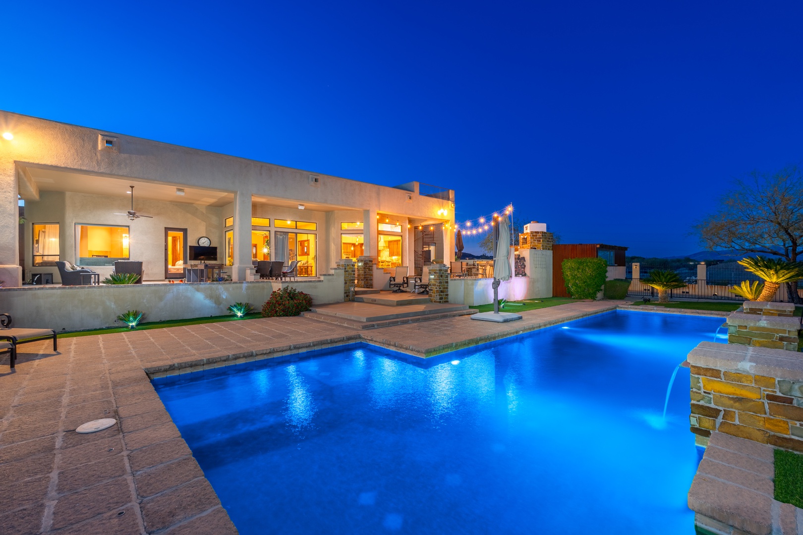 A stunning evening view showcasing the property's illuminated pool and spacious patio area against the desert landscape backdrop at twilight.