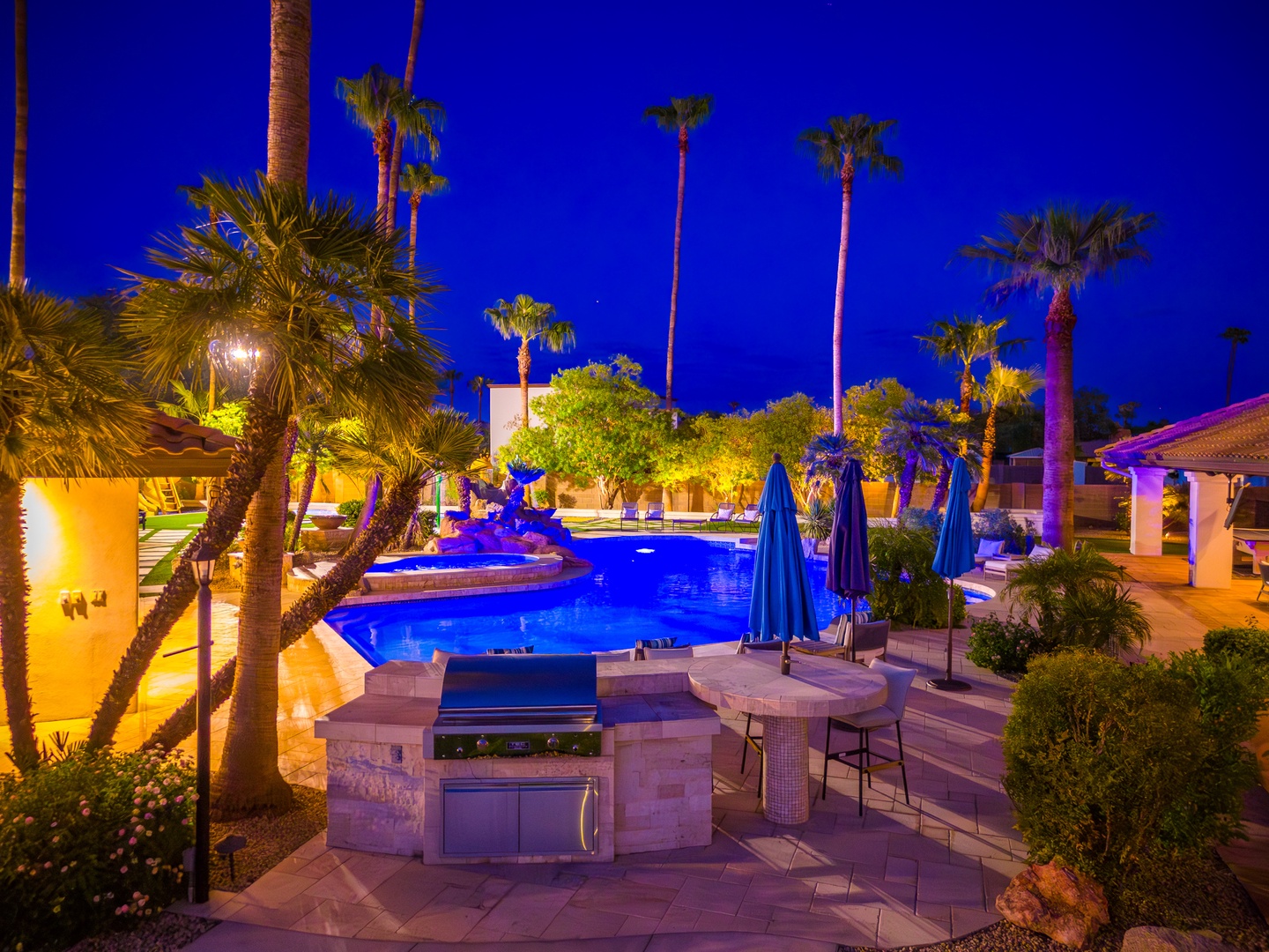 This stunning resort-style backyard features a glowing pool, outdoor kitchen, and palm trees under twilight skies—your private paradise awaits for evening gatherings and relaxation.