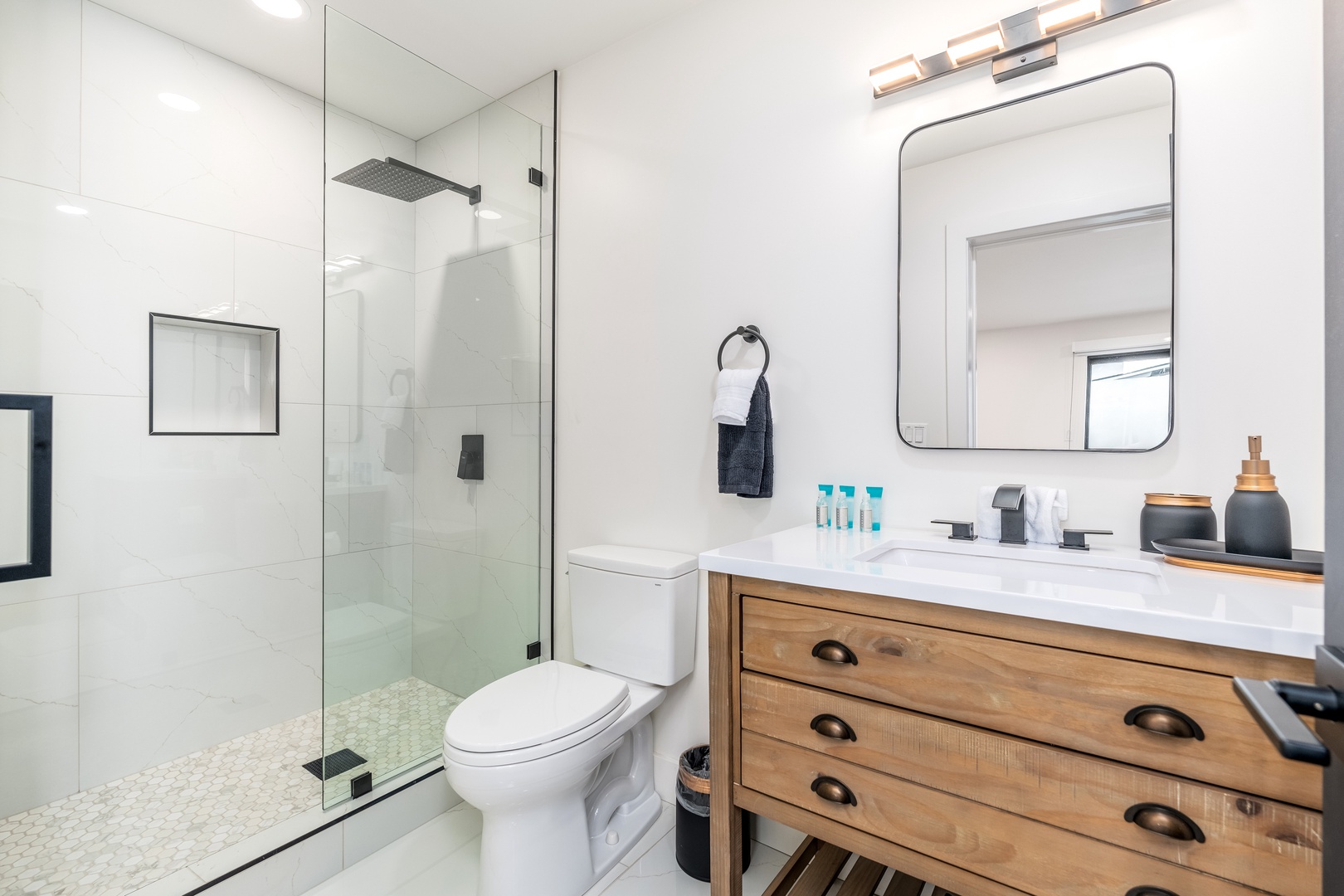 Step into this bright, spa-like bathroom with its crisp white tiles, spacious walk-in shower, and beautifully crafted wood vanity—your personal retreat awaits.