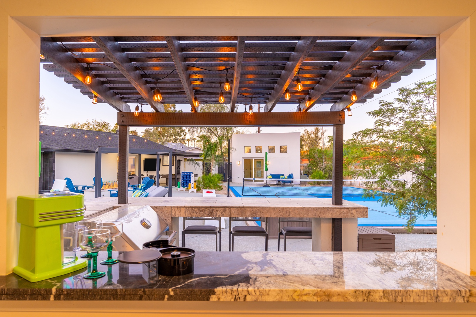 Your outdoor kitchen opens to a stunning covered patio with ambient lighting, perfect for preparing meals while enjoying pool and garden views in the warm evening air.