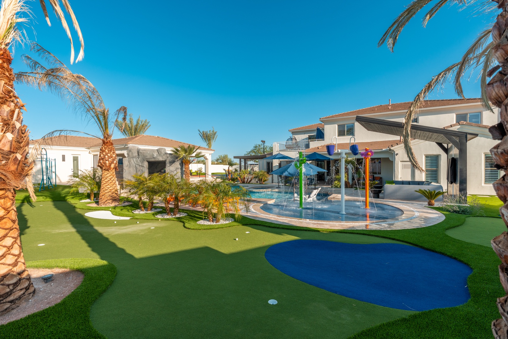 A sprawling resort-style property framed by mature palms offers a putting green, splash pad, and pool—perfect for creating unforgettable family memories under sunny skies.