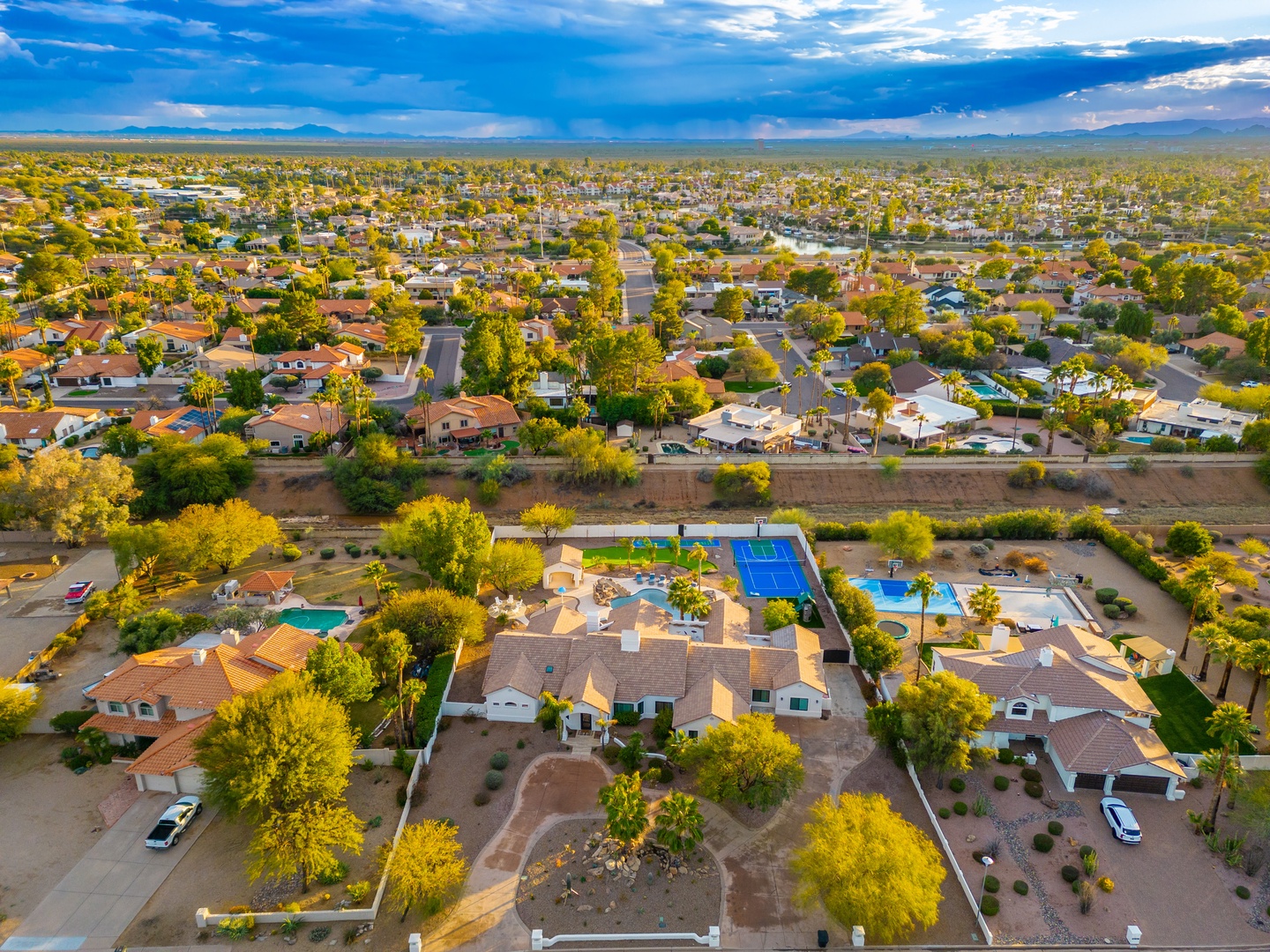 Aerial view of the vacation rental property showcasing swimming pools, tennis court, and expansive grounds in a quiet residential neighborhood with mountain views.