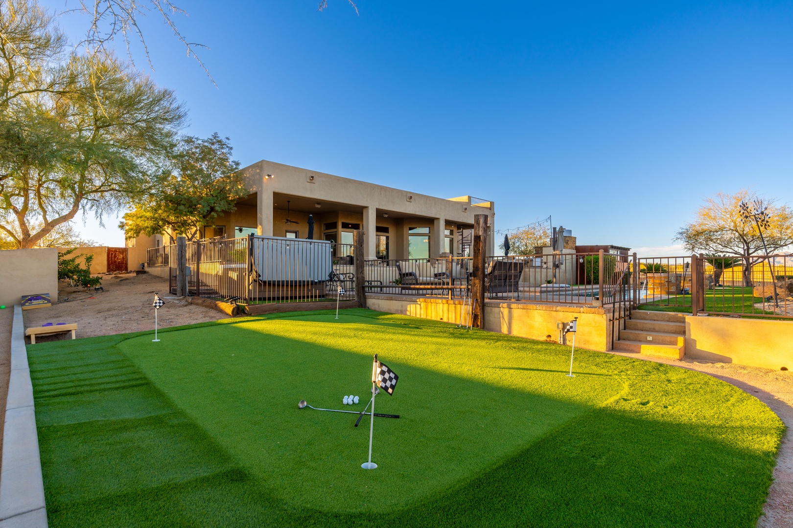 The property features a private putting green beneath open skies, surrounded by mature trees and bordered by a modern covered patio—ideal for outdoor leisure and desert evenings.