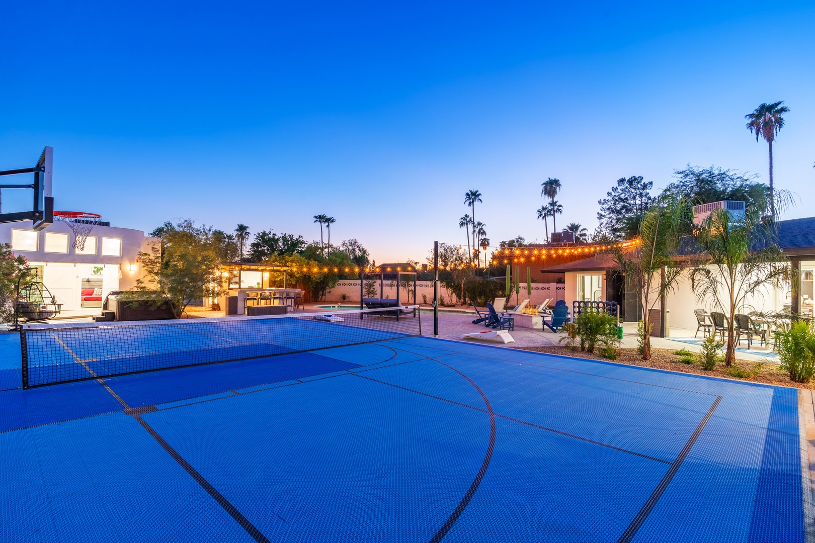 A private sports court lit by string lights and palm trees creates the perfect setting for friendly games under desert skies, with lounging areas nearby for relaxing afterward.