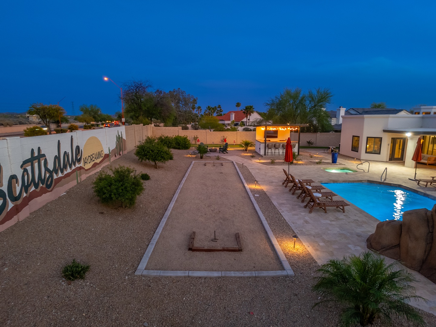 The property features an illuminated pool, bocce ball court, and modern outdoor spaces—ideal for evening relaxation and group gatherings in the surrounding desert neighborhood.