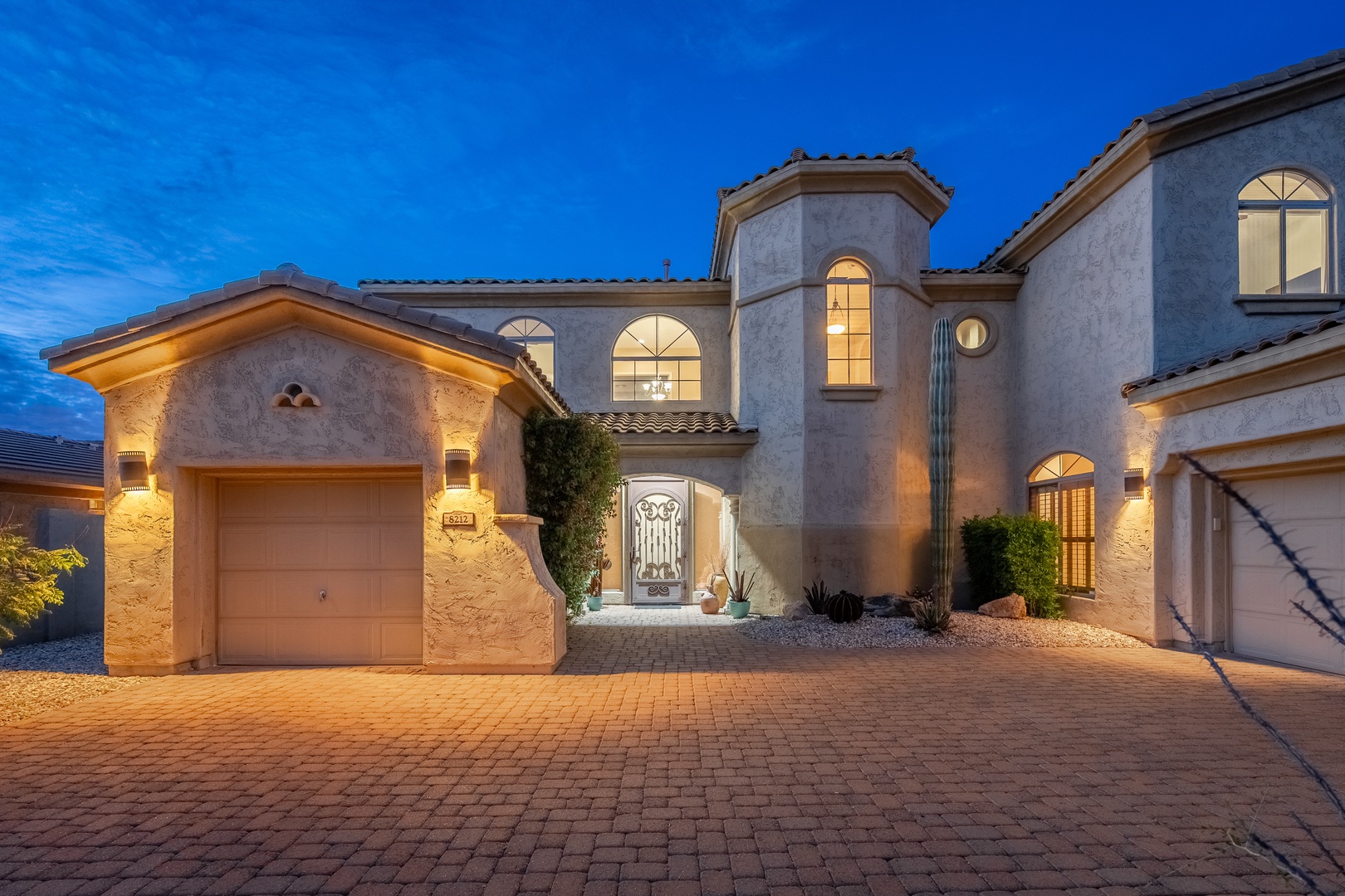 Stunning Mediterranean-style villa illuminated at twilight, showcasing elegant architecture and desert landscaping in a peaceful residential neighborhood.