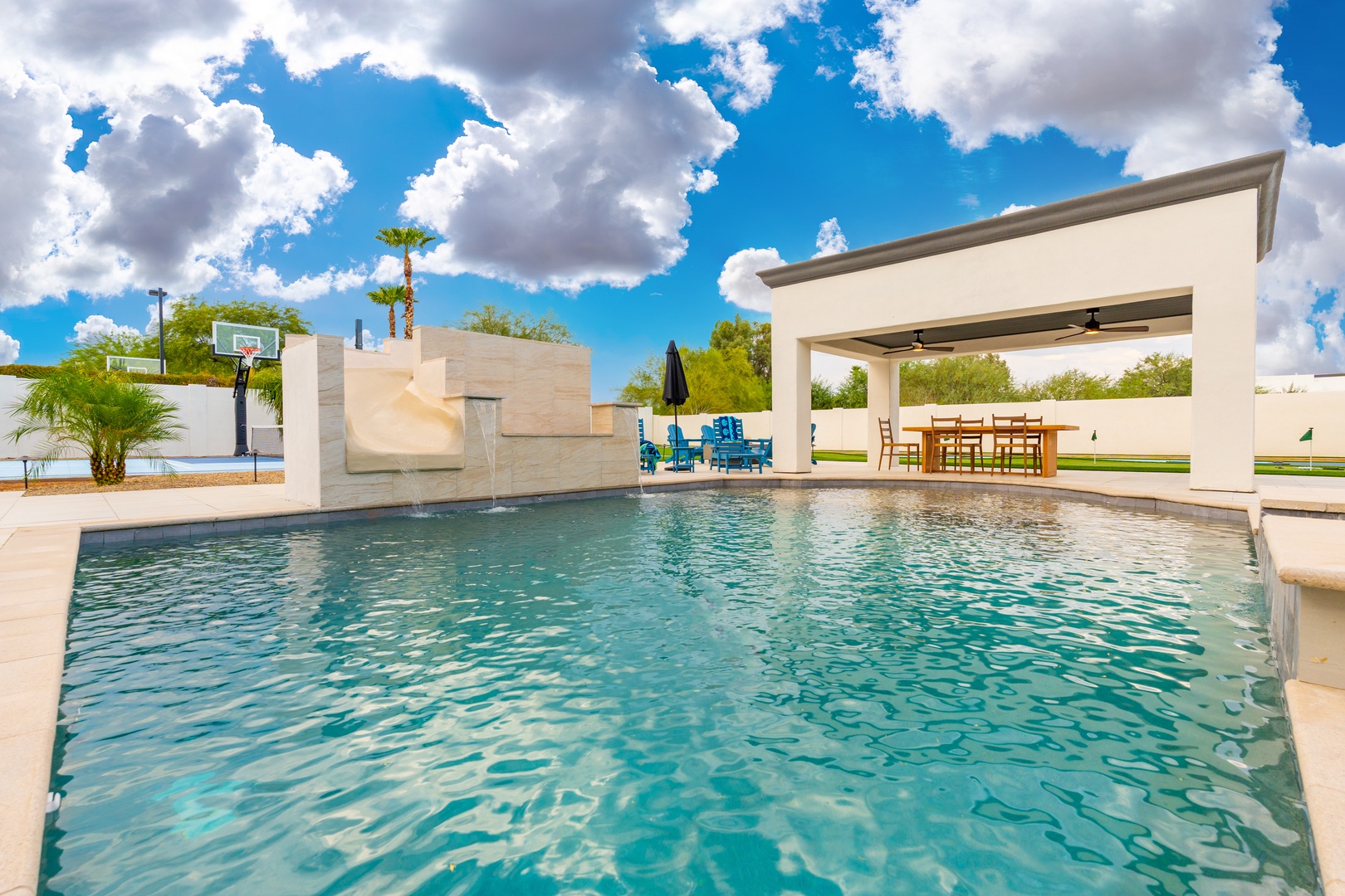 A sparkling pool anchors this modern oasis, framed by sleek architecture, a covered dining pavilion, and a basketball court—perfect for sun-soaked days and effortless outdoor entertaining.