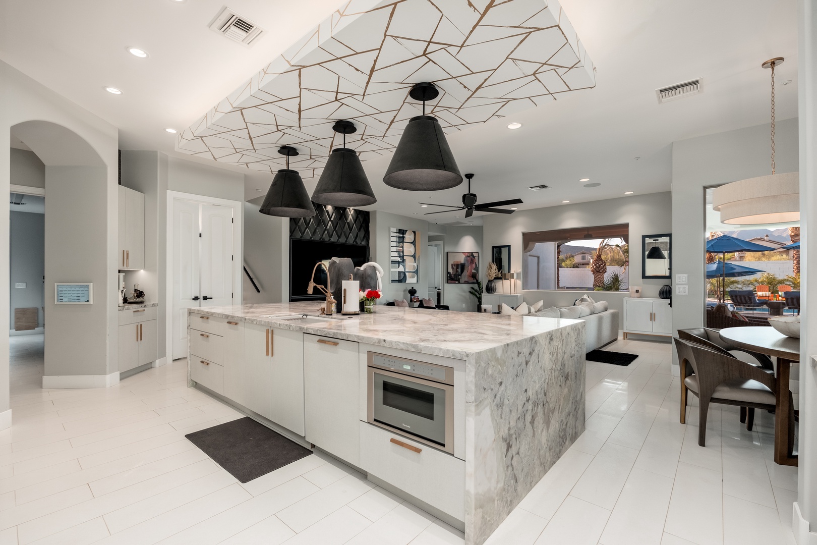 A stunning modern kitchen with white cabinetry, luxurious marble countertops, and a striking geometric ceiling design creates a sophisticated culinary space. Elegant pendant lighting and seamless flow into the living and outdoor areas enhance your comfort