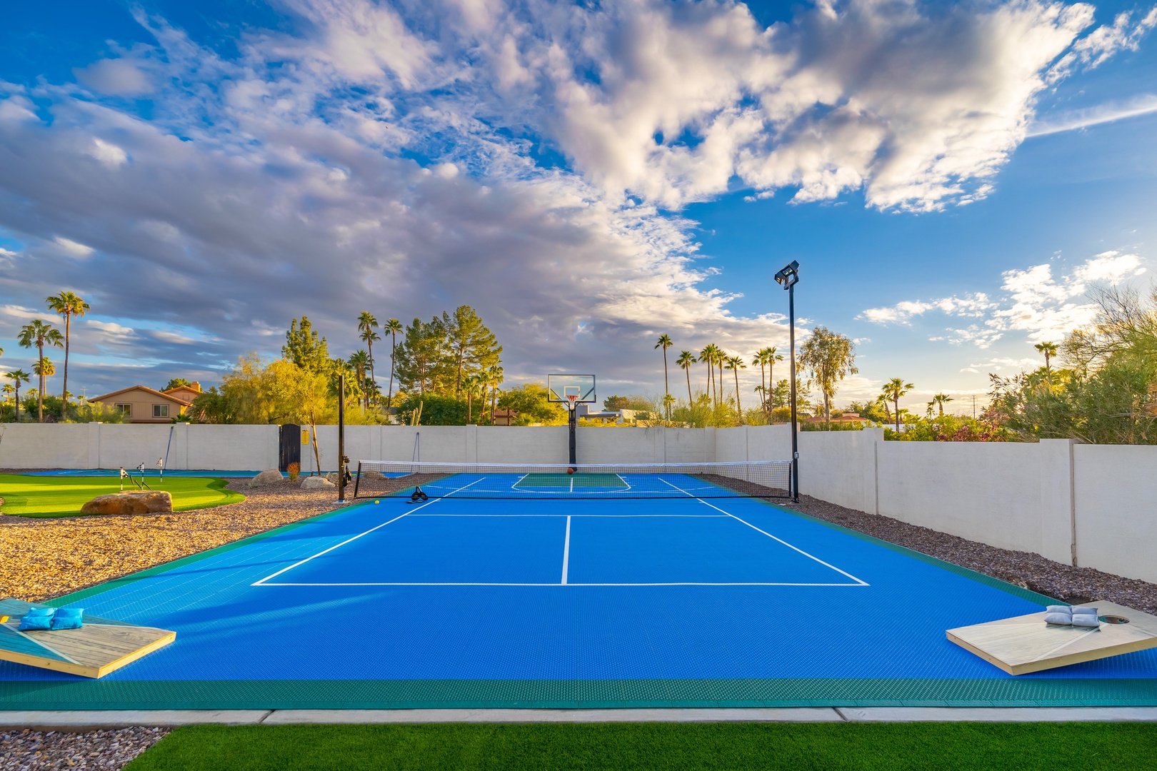 A vibrant blue private tennis court complete with basketball hoop awaits your friendly match, framed by swaying palms and dramatic desert skies.
