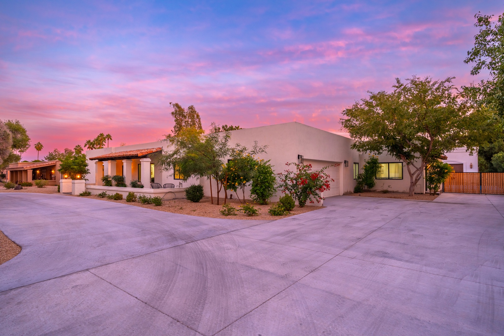 Stunning desert retreat bathed in a vibrant pink and purple sunset, surrounded by mature landscaping and palm trees, welcoming guests to their Southwest escape.