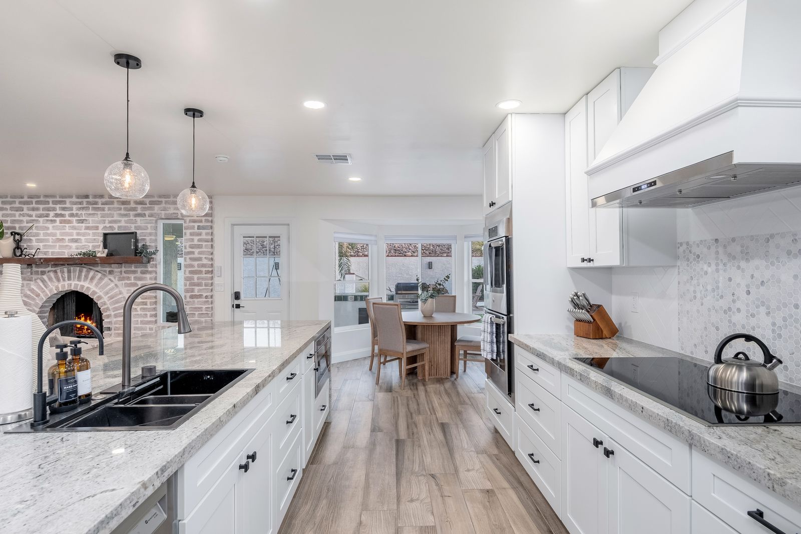 Cook with ease in this spacious, chef-inspired kitchen featuring premium appliances, elegant white cabinetry, and a charming brick fireplace that adds warmth to your culinary adventures.