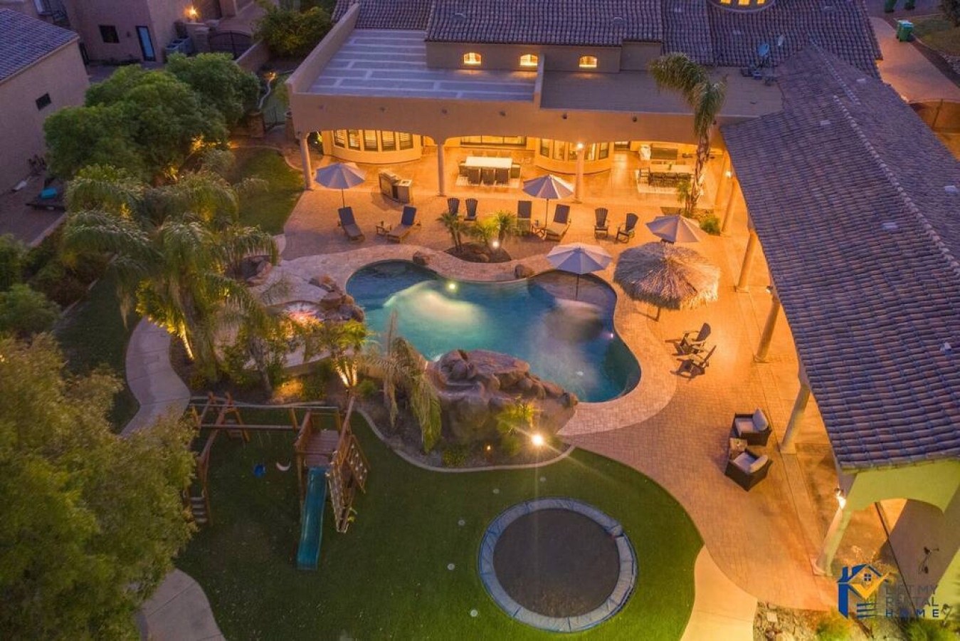 Aerial view showcases this stunning property featuring a beautiful curved swimming pool with integrated spa, expansive patio areas, and tropical landscaping with mature palm trees.