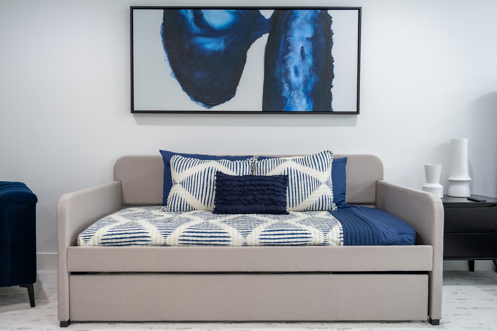 Sink into this inviting daybed with its elegant upholstered frame and bold abstract artwork above. The crisp blue-and-white bedding and thoughtful design create a cozy retreat where you can unwind in style.