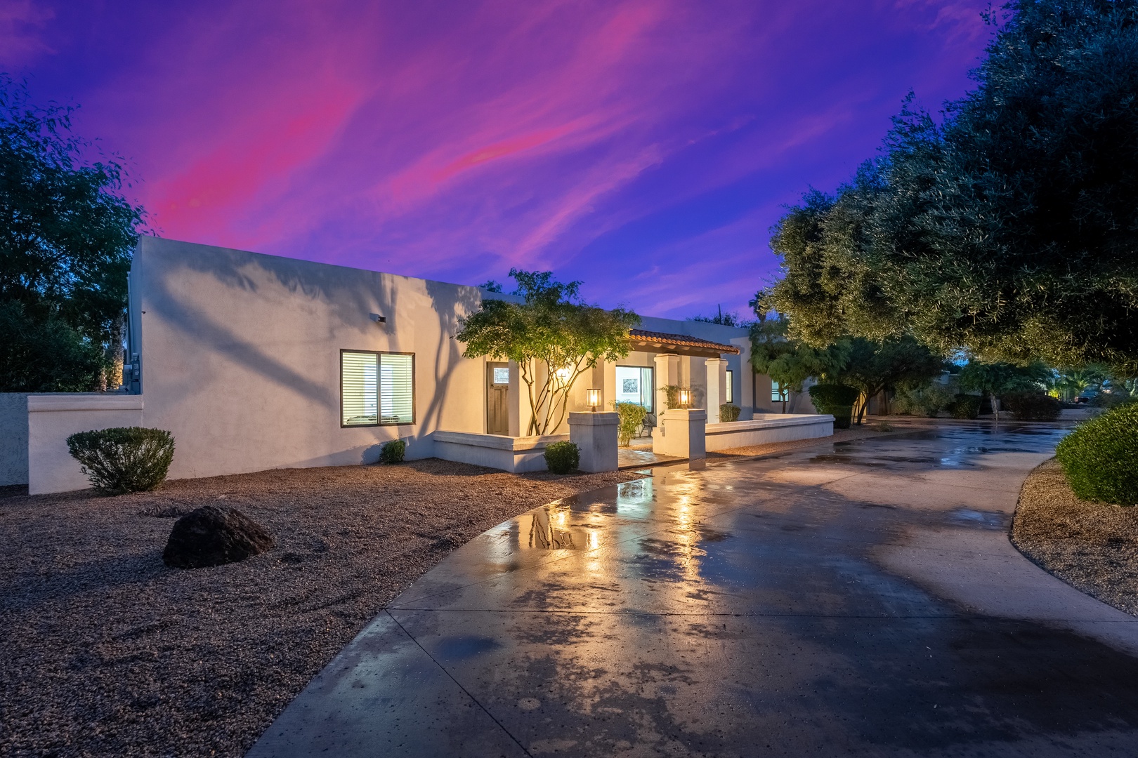 Stunning desert retreat featuring modern architecture beneath a dramatic purple and pink twilight sky, surrounded by mature landscaping and natural desert foliage.