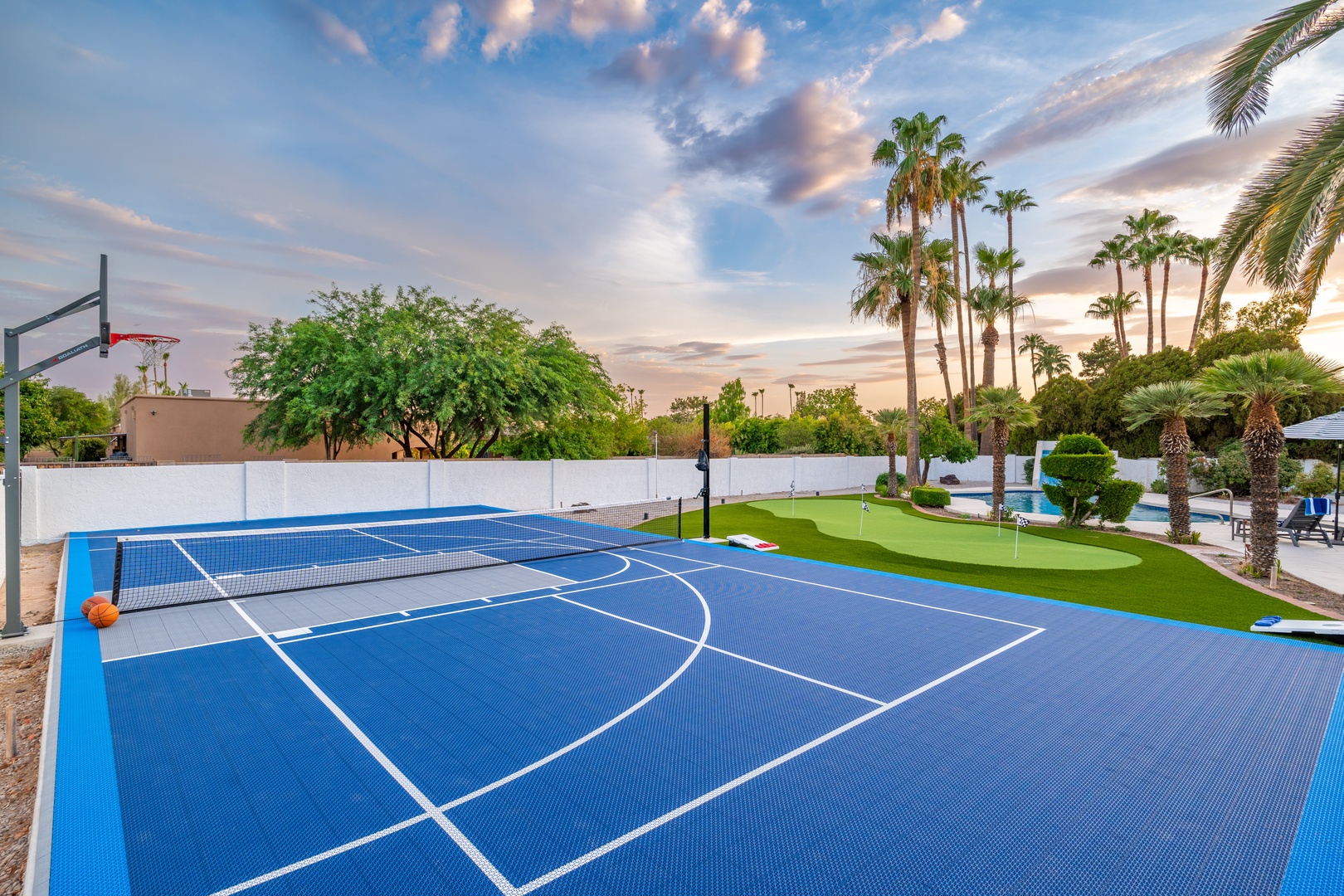 An outdoor sports court framed by towering palm trees and a mini-golf green, set against a stunning sunset sky—perfect for active evenings in a tropical setting.
