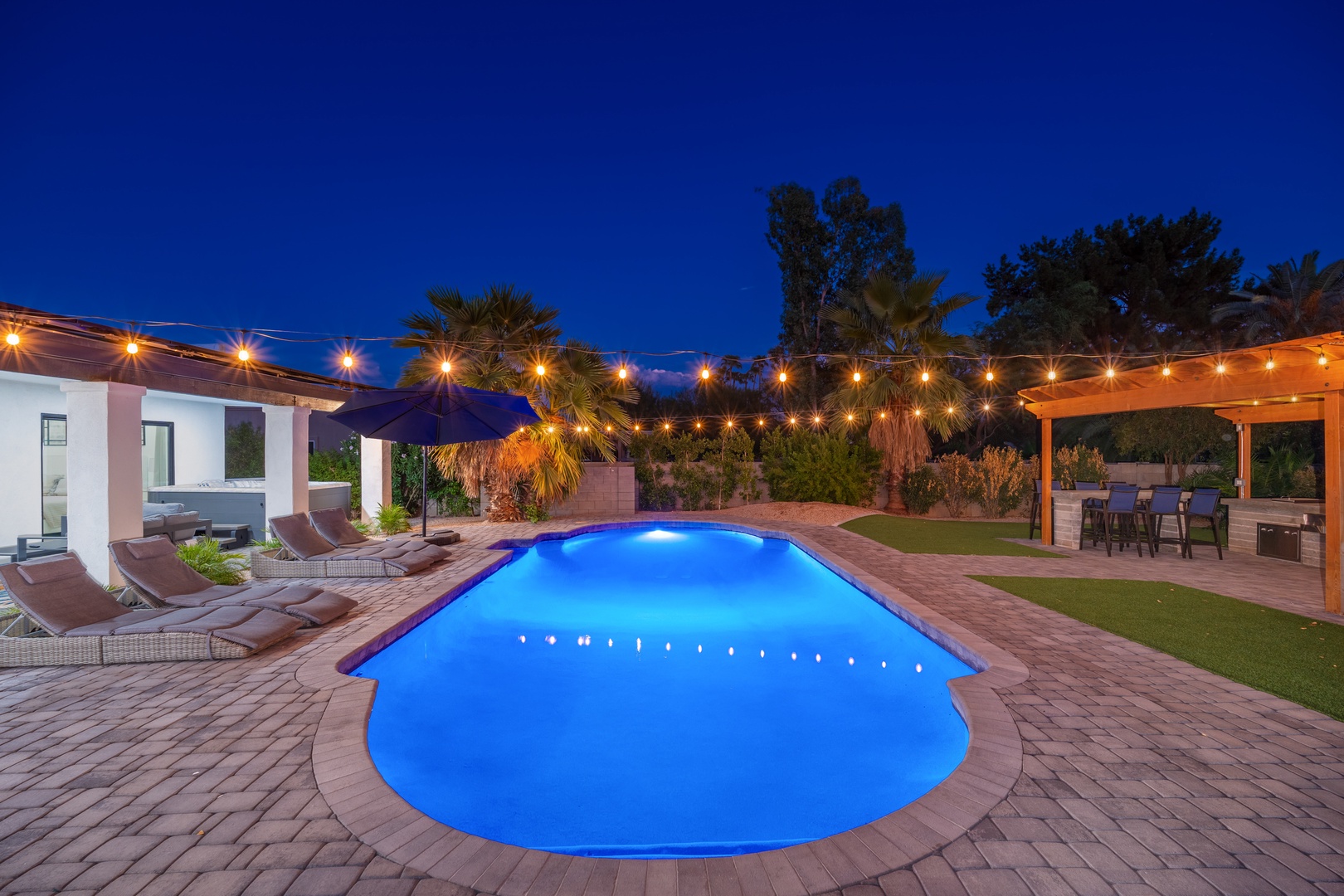 Unwind under starlit skies in your private backyard oasis, where the glowing pool beckons for evening swims and the lit patio invites you to dine under string lights surrounded by palm trees.