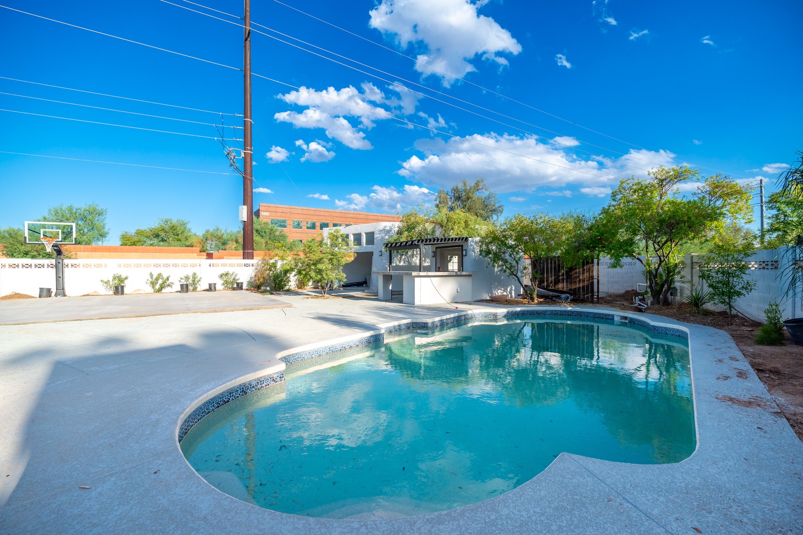 The property features a large private pool surrounded by an expansive backyard area with a full-size basketball court, perfect for outdoor recreation under sunny desert skies.