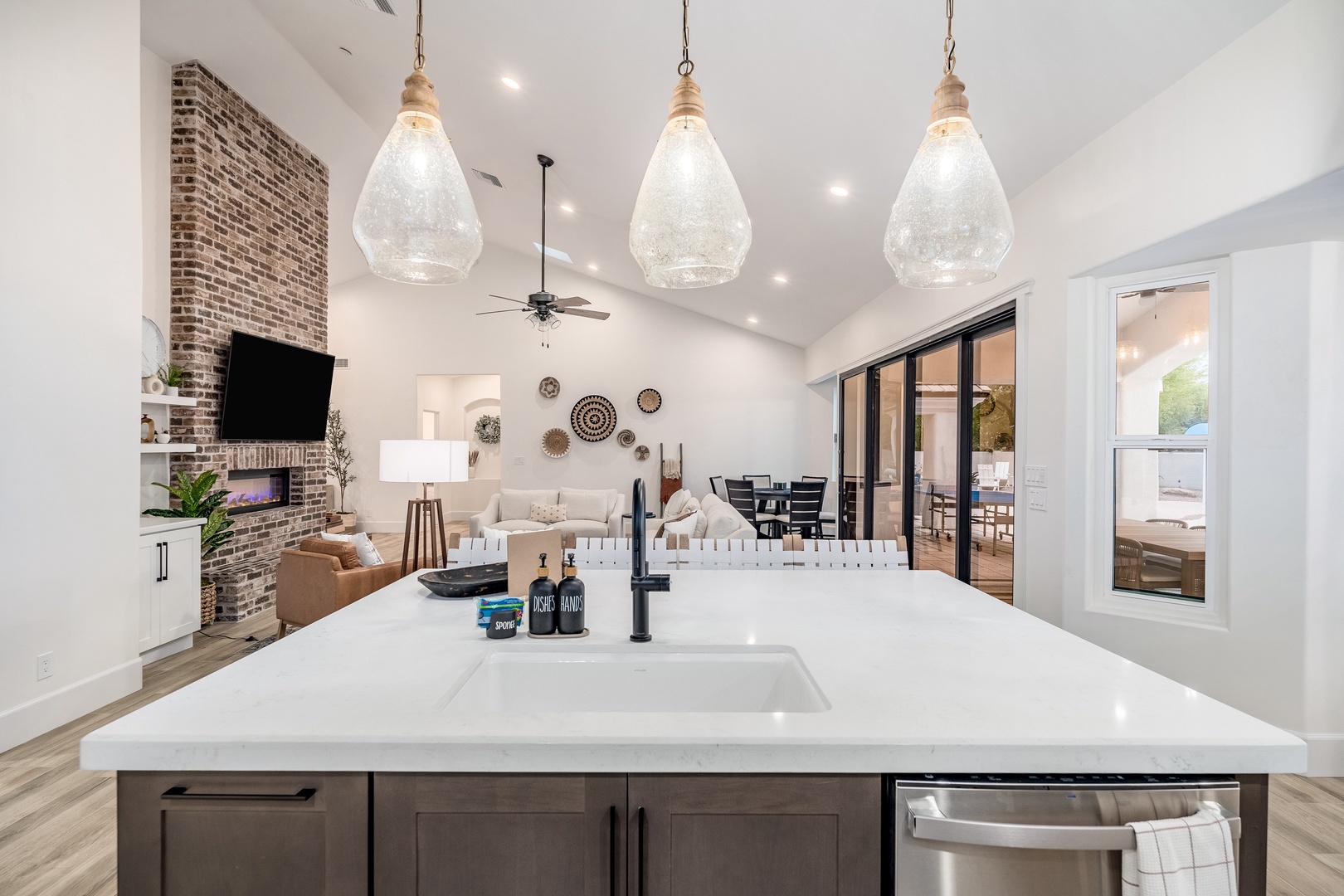 Step into your open living space where soaring ceilings meet a statement brick fireplace, stylish pendant lighting illuminates your chef's kitchen, and seamless access to your outdoor patio invites effortless indoor-outdoor living.