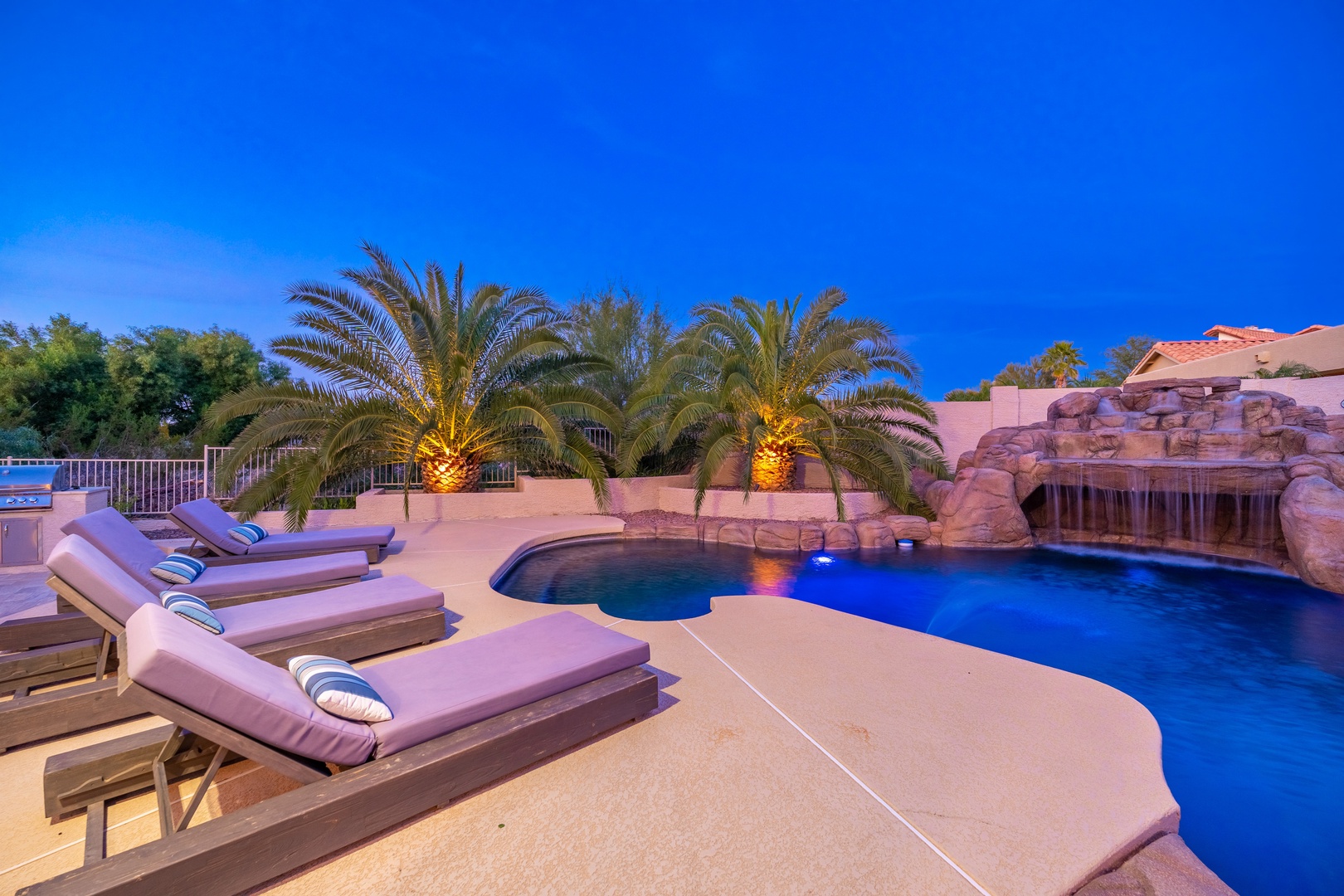 Soak up the desert sun on plush loungers beside your private pool, with a stunning rock waterfall and swaying palms creating your own backyard oasis under a brilliant blue sky.