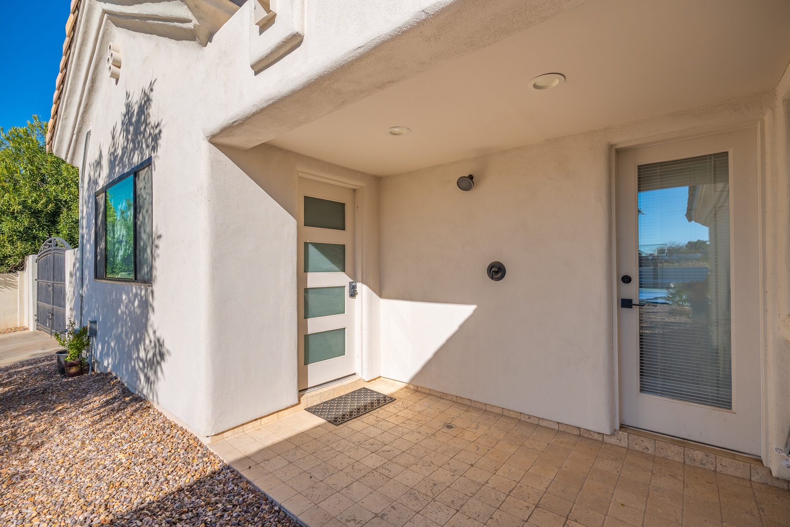 Modern white stucco exterior with covered entryway, glass-paneled door, and clean architectural lines under bright blue skies—a welcoming first glimpse of your vacation retreat.