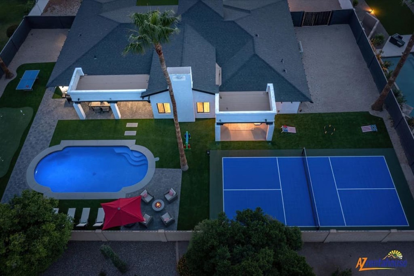 Modern vacation villa with private pool and tennis court in residential setting, captured at twilight.
