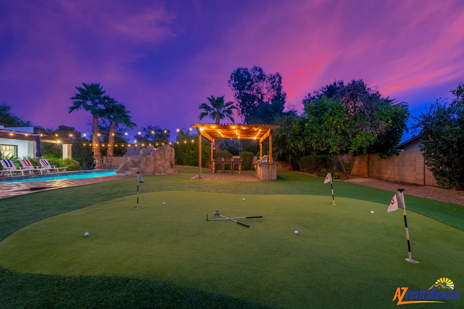 Spectacular backyard features a private putting green beneath dramatic purple skies, with pool and covered dining area creating the perfect desert oasis.