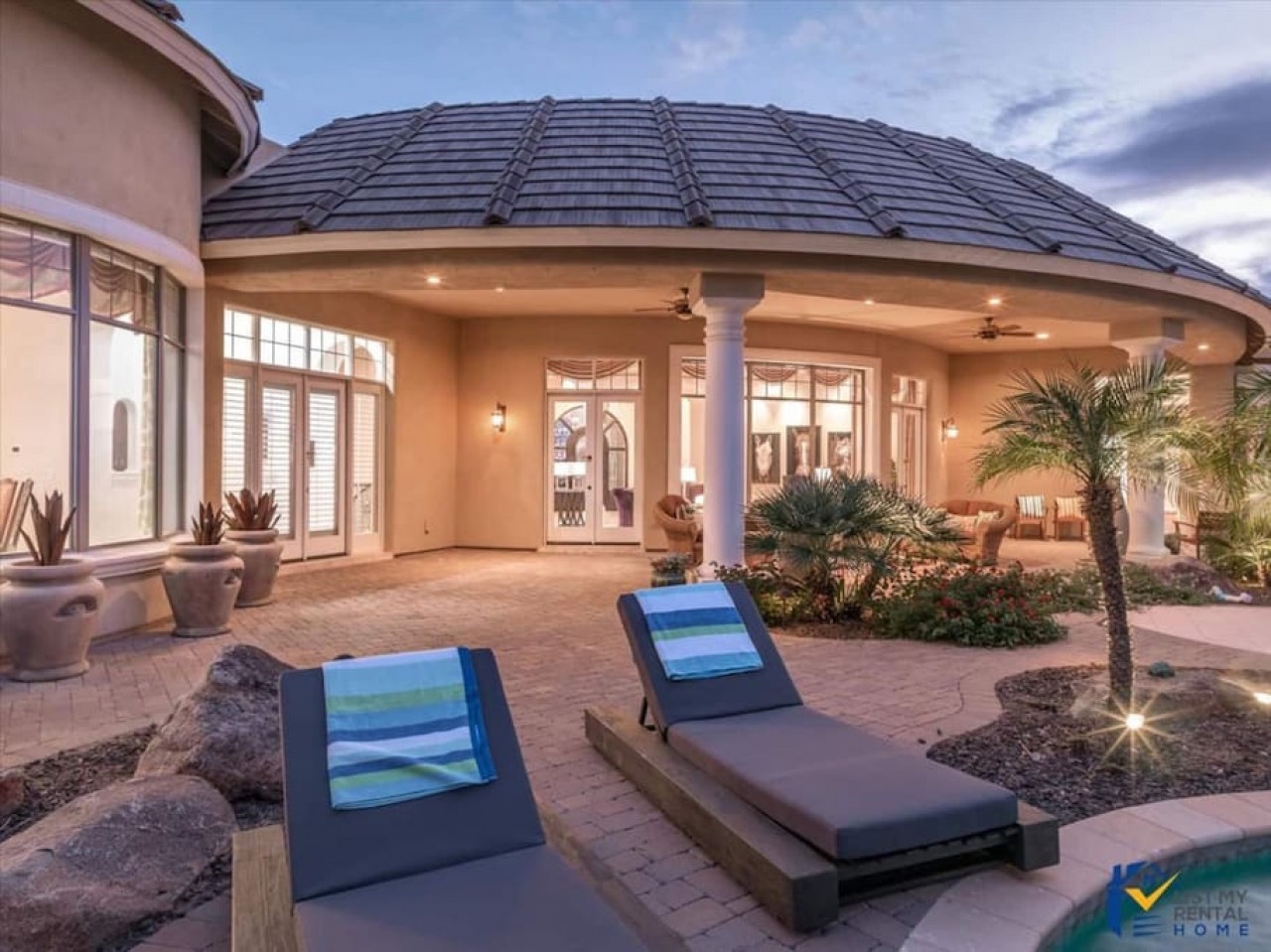 Elegant vacation home featuring outdoor loungers and tropical landscaping under a distinctive curved roof design.