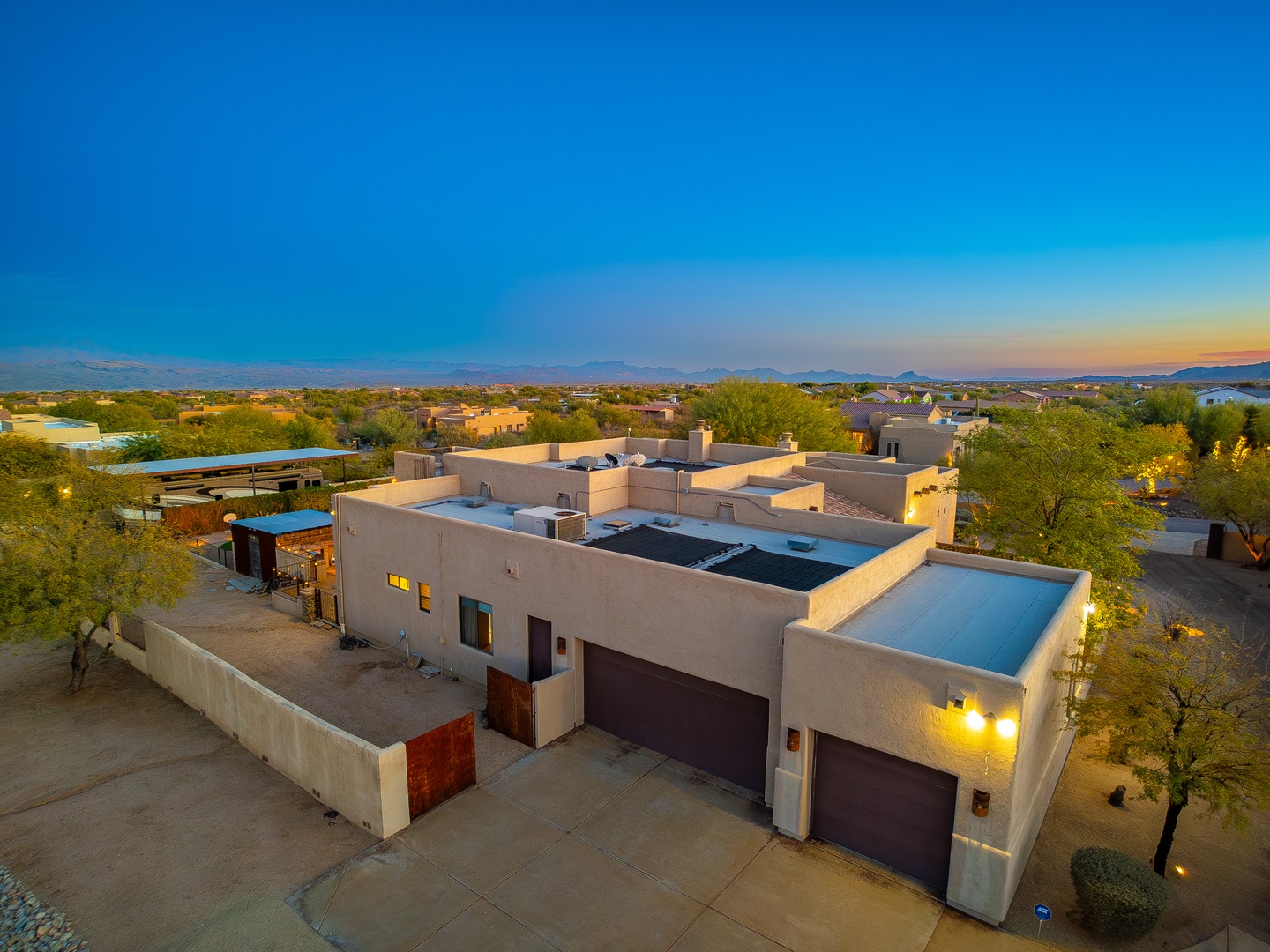 Aerial view captures the property's contemporary architecture nestled in a scenic desert neighborhood, framed by mountain ranges and softly lit at dusk.