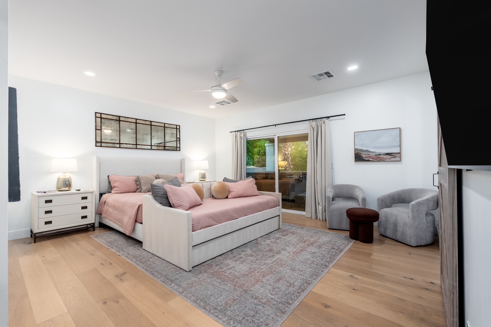 Sink into this serene bedroom where soft pink bedding meets plush seating. Glass doors open to your private patio, inviting natural light to dance across warm wood floors.