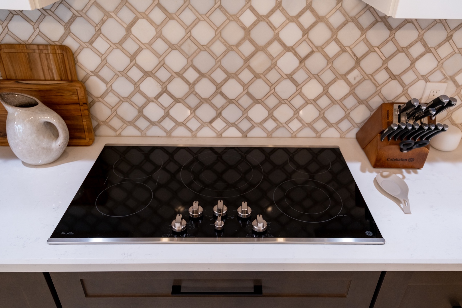 A sleek electric cooktop awaits your culinary adventures, with elegant knife set and charming décor adding warmth to this well-appointed kitchen space.