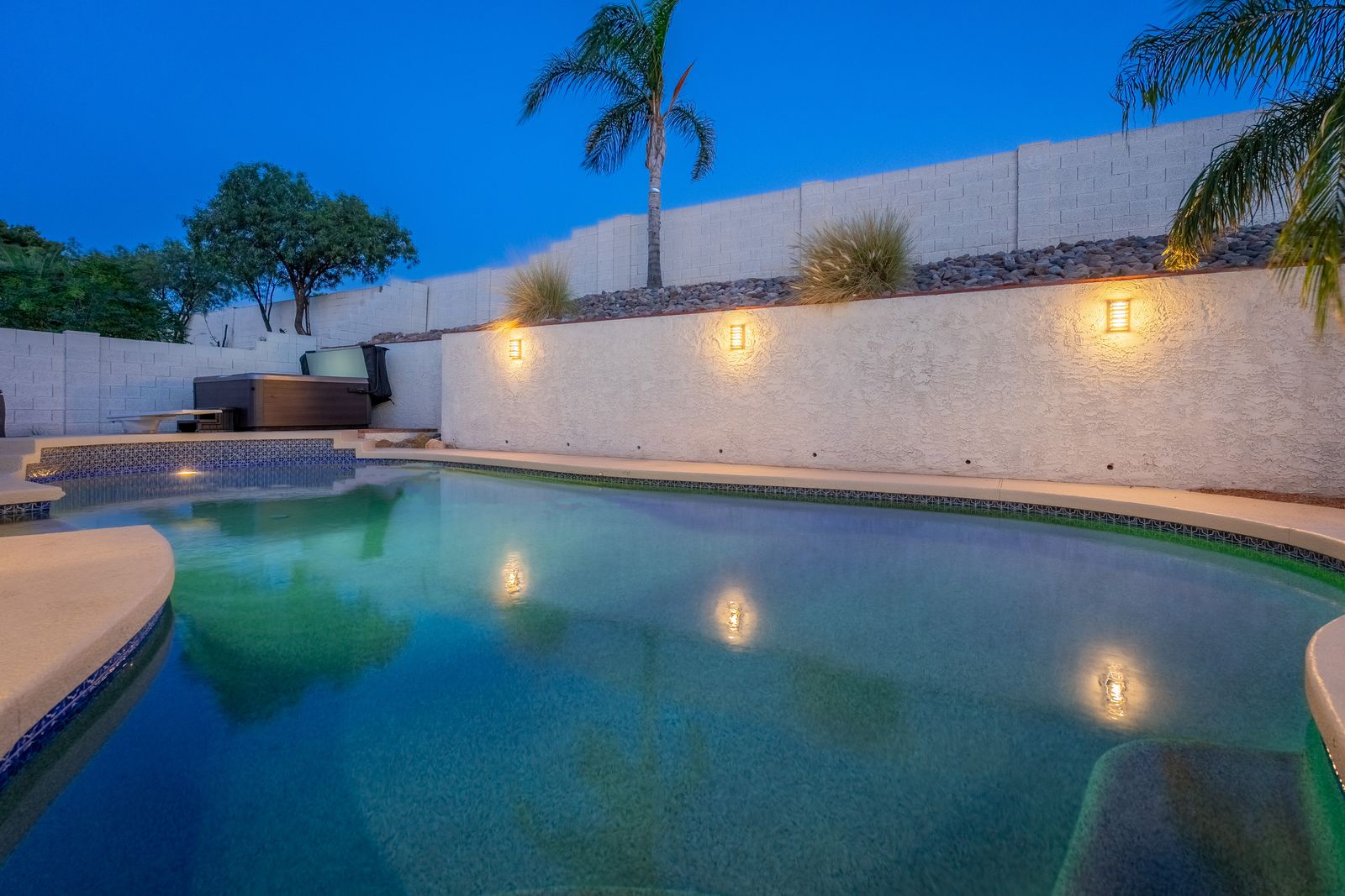 Your private pool glows under ambient lighting, with a hot tub nestled beside it and swaying palms overhead—perfect for warm evenings under the stars.
