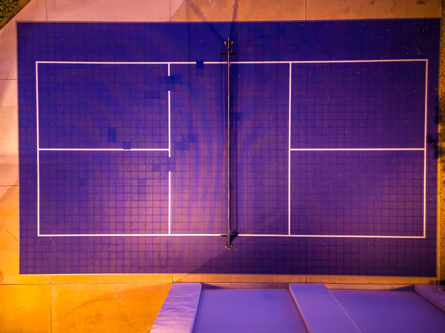 A vibrant aerial view of the property's tennis court with striking purple surface and pink surrounding areas, perfect for active recreation.