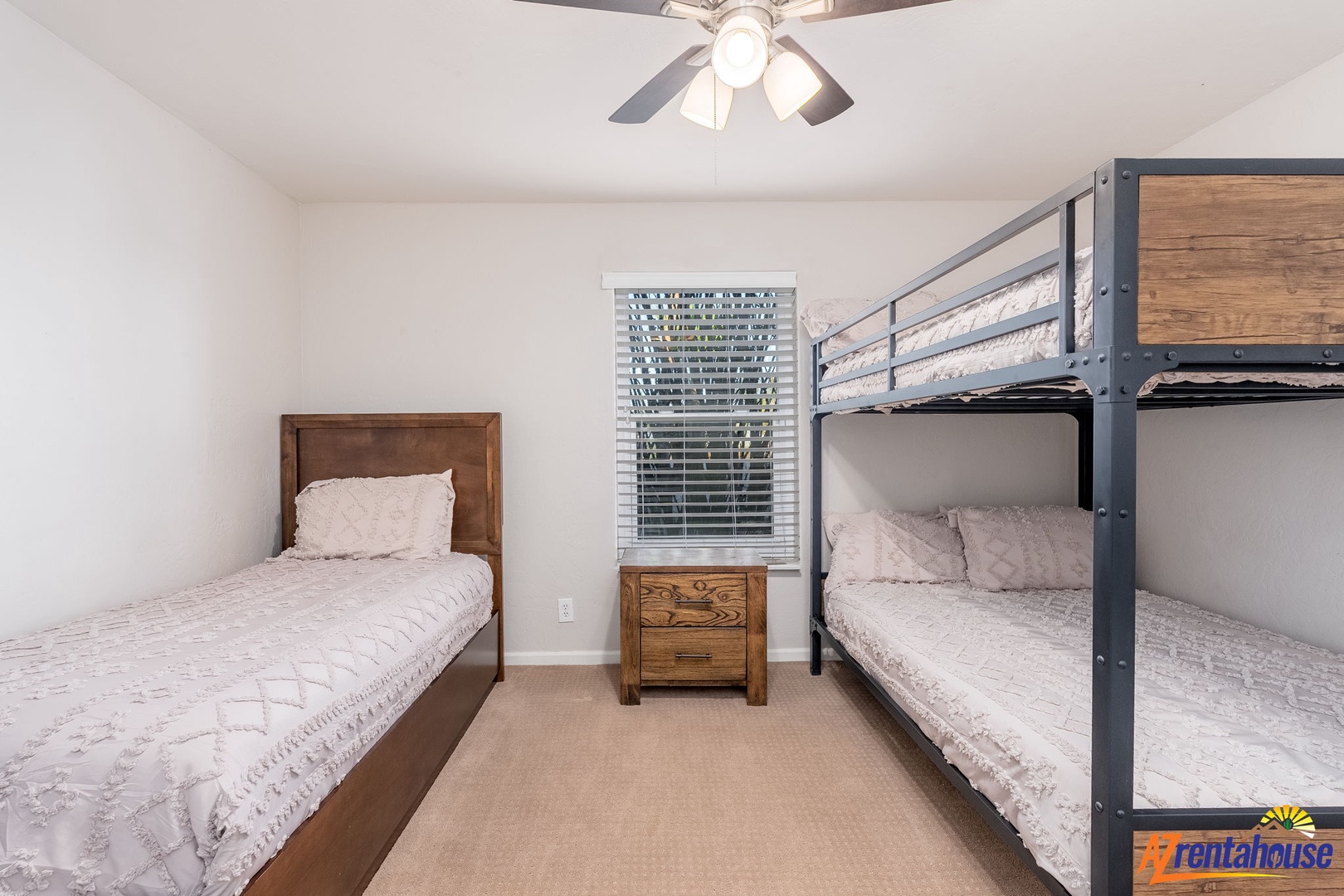 Your group will sleep soundly here—a cozy bunk and twin bed setup with soft linens, warm wood tones, and a ceiling fan to keep you comfortable all night long.