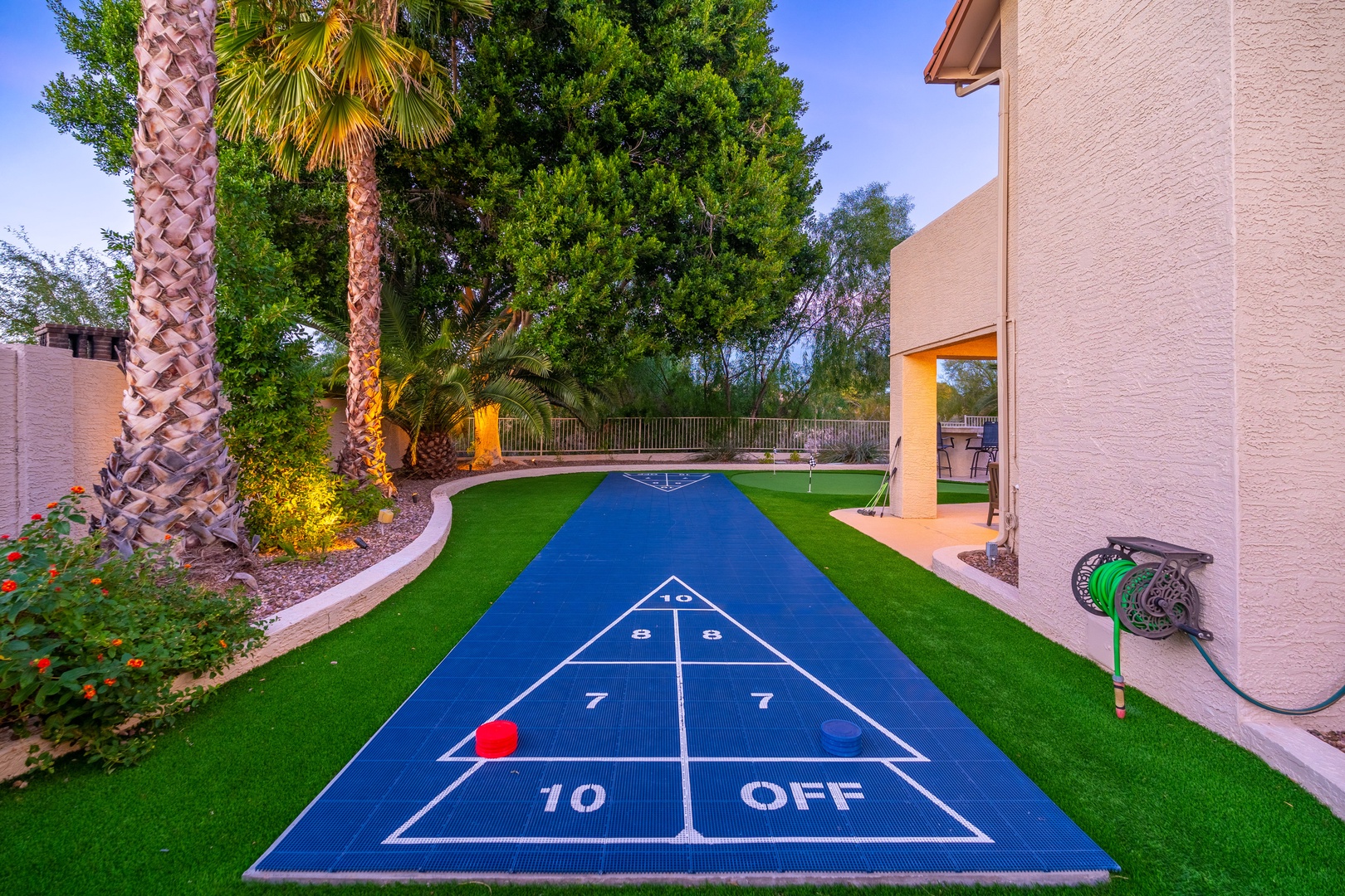 This property features a private shuffleboard court nestled in a lush, landscaped backyard surrounded by palm trees and mature greenery.