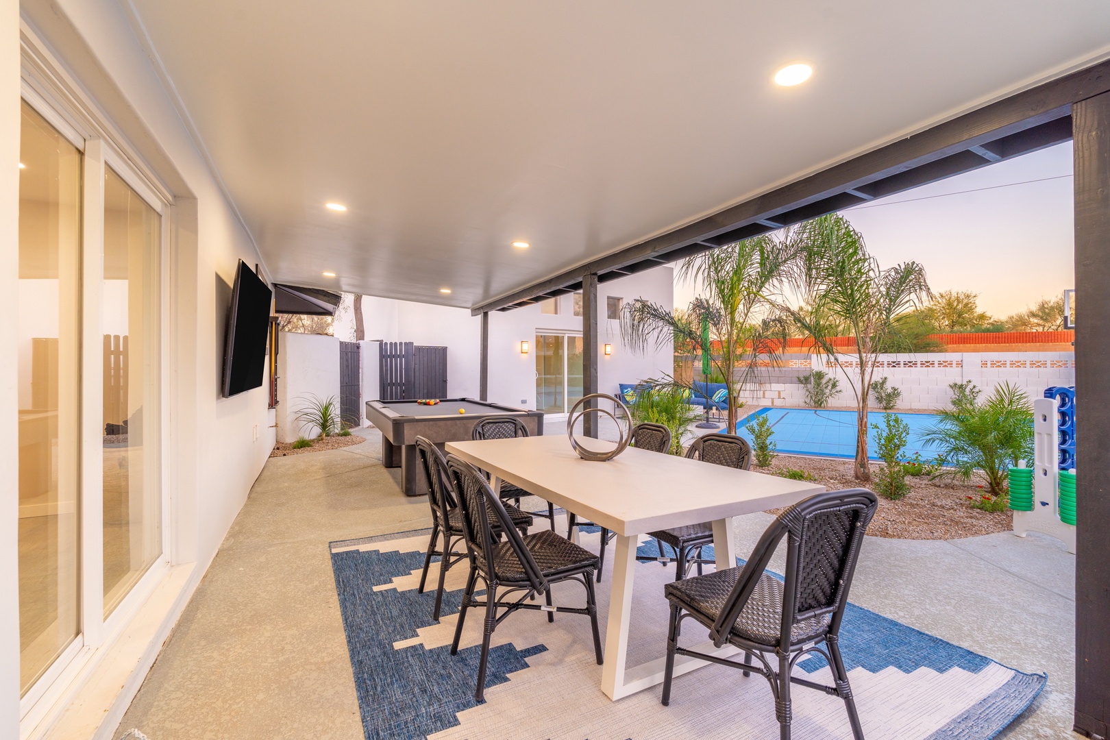 Gather around your covered patio table for meals with pool views, while a billiards table awaits for friendly competition under modern outdoor lighting.