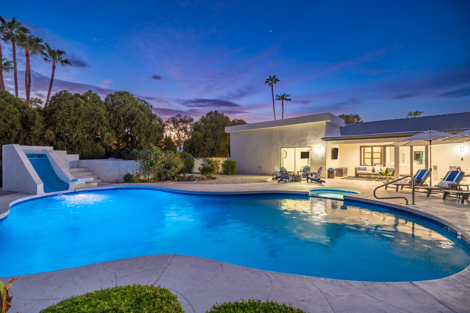 A stunning desert retreat framed by swaying palms and dusky skies, this property features a sparkling pool with a built-in slide and ample space for outdoor gatherings.