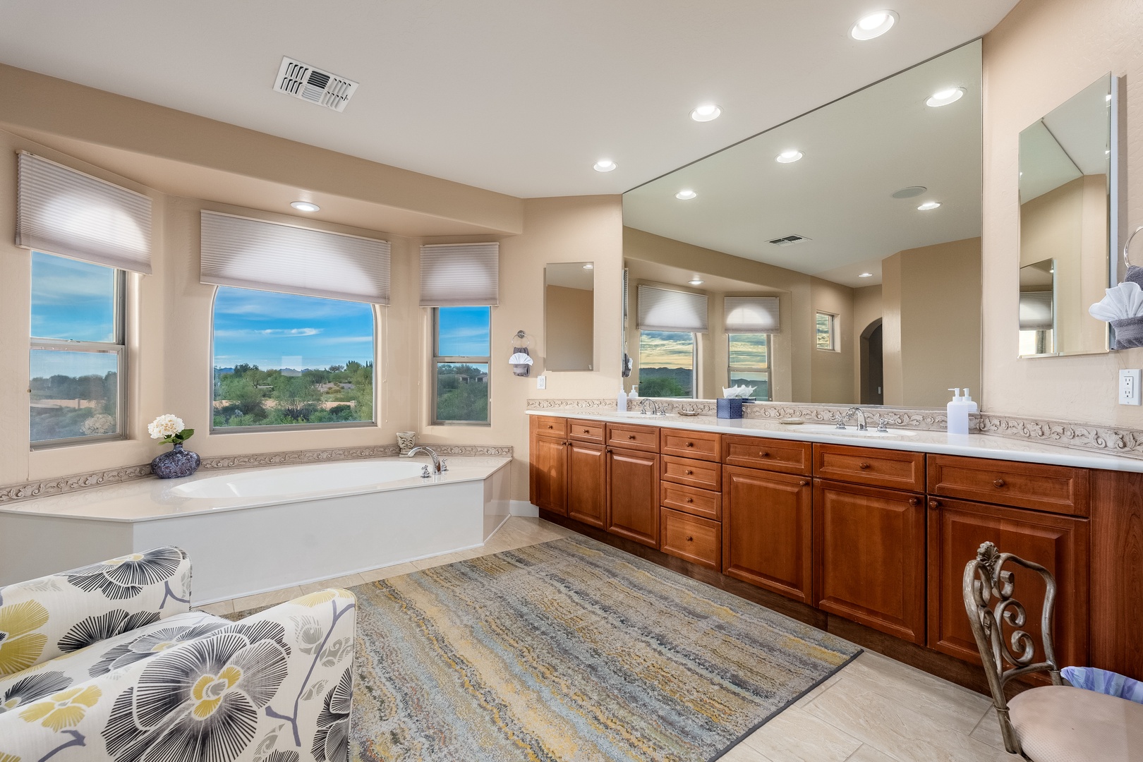 Soak in your spa-like master bath featuring a soaking tub framed by views, dual vanities with elegant granite, warm wood cabinetry, and serene natural light.