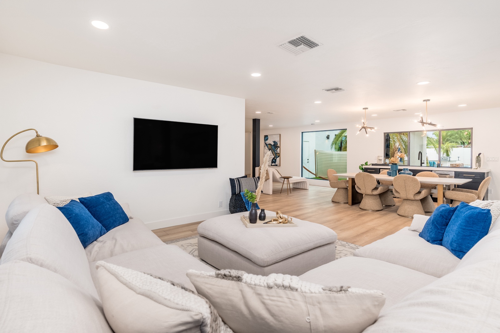 Sink into plush white sofas with vibrant blue pillows as you unwind in this bright, open living space. Sunlight pours through the windows, connecting you to the inviting dining area beyond.