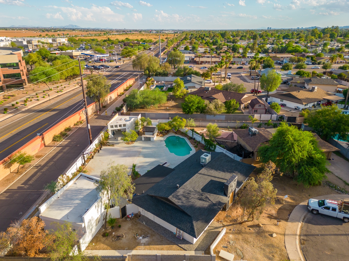 Aerial view of the property situated in a residential neighborhood with nearby shopping and dining conveniences, surrounded by palm-lined streets and open desert landscapes.